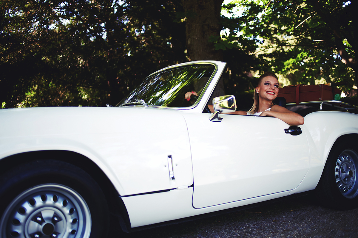 Successful and wealthy woman sitting behind the wheel of her luxury cabriolet car on countryside feeling happy,young smiling female sits in her new convertible car outdoors enjoying the life in summer